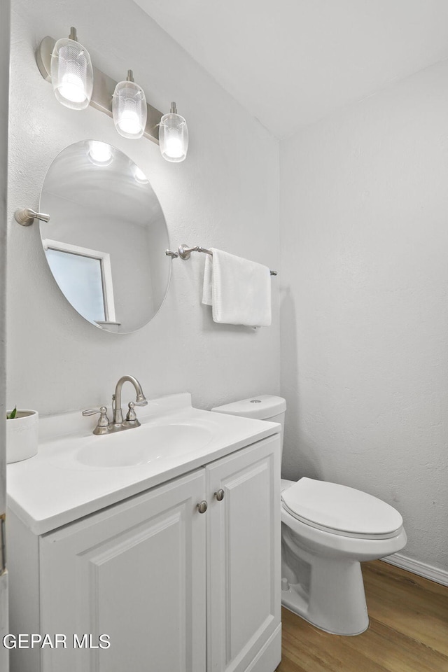 half bathroom featuring vanity, toilet, baseboards, and wood finished floors