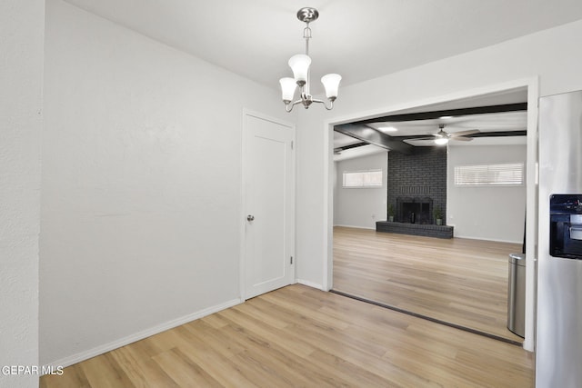 unfurnished dining area featuring a fireplace, ceiling fan with notable chandelier, baseboards, and light wood-style floors