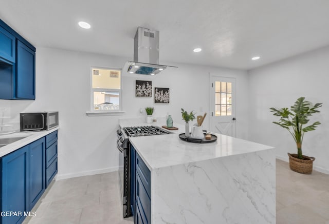 kitchen with island exhaust hood, blue cabinetry, light stone counters, and stainless steel gas range