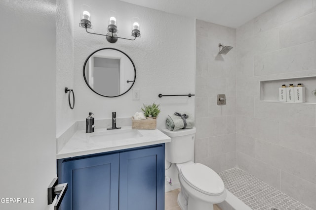 bathroom with a tile shower, vanity, and toilet