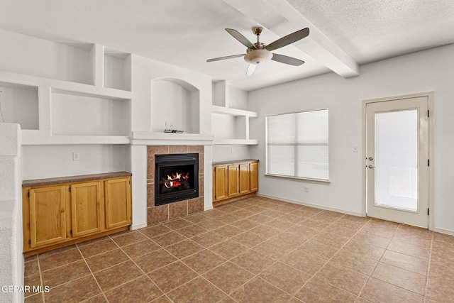 unfurnished living room featuring a textured ceiling, a tiled fireplace, ceiling fan, beam ceiling, and tile patterned flooring