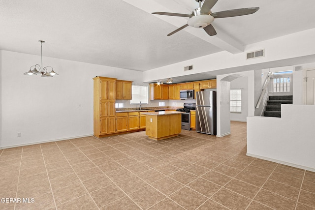 kitchen with beam ceiling, a kitchen island, stainless steel appliances, ceiling fan with notable chandelier, and decorative light fixtures