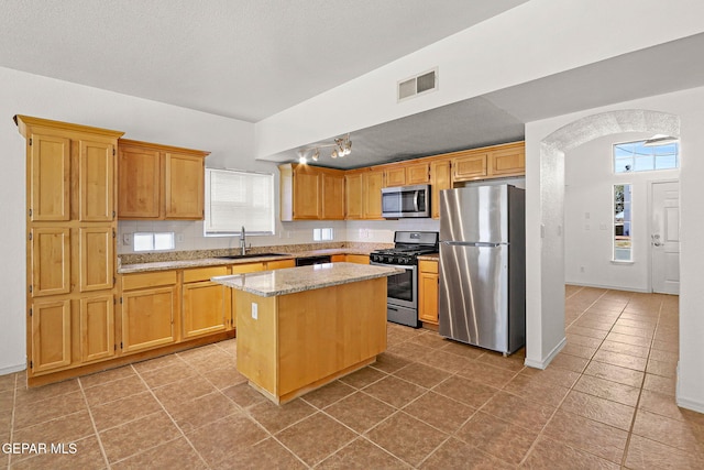 kitchen with a kitchen island, sink, light tile patterned flooring, appliances with stainless steel finishes, and light stone counters