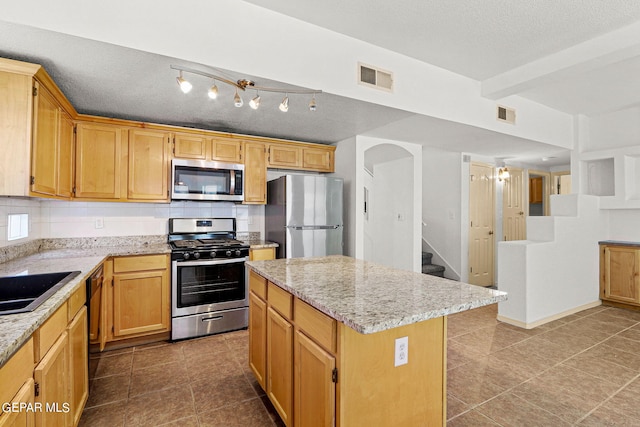 kitchen featuring backsplash, appliances with stainless steel finishes, a kitchen island, a textured ceiling, and tile patterned floors