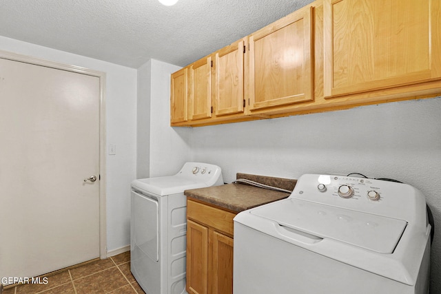 clothes washing area with cabinets, a textured ceiling, washing machine and clothes dryer, and dark tile patterned flooring