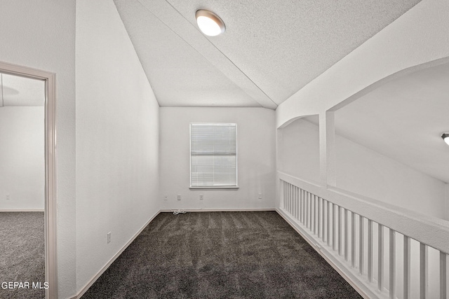 additional living space featuring dark carpet, vaulted ceiling, and a textured ceiling