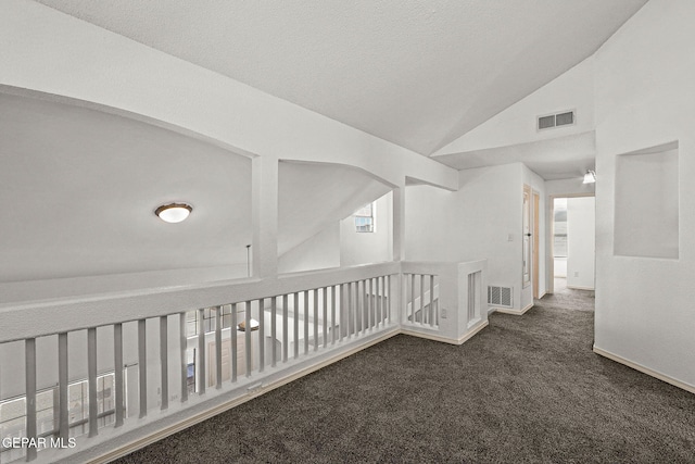 hallway with vaulted ceiling and dark colored carpet