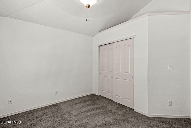 unfurnished bedroom featuring a closet, lofted ceiling, and dark colored carpet