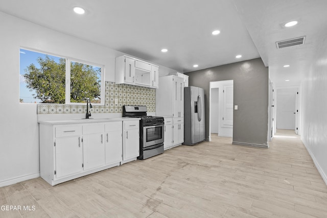 kitchen with white cabinets, sink, appliances with stainless steel finishes, light hardwood / wood-style floors, and decorative backsplash