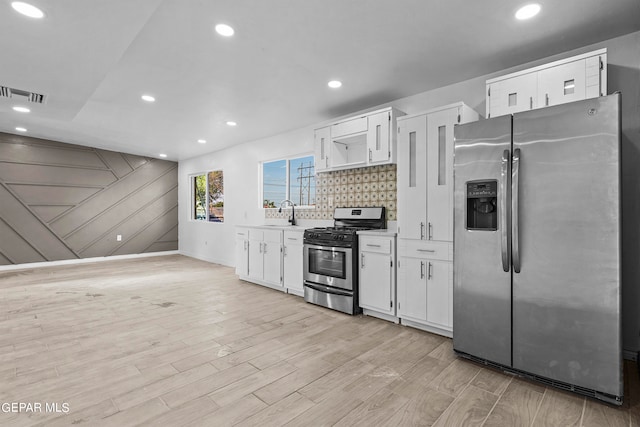 kitchen featuring light wood-type flooring, stainless steel appliances, white cabinets, sink, and backsplash