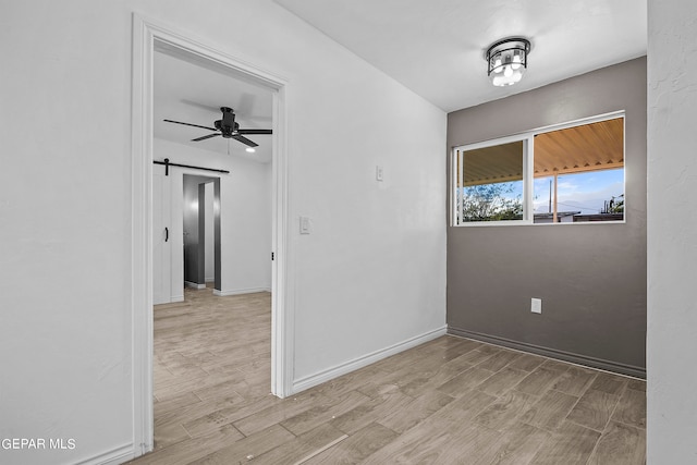 empty room featuring ceiling fan, a barn door, and light hardwood / wood-style flooring