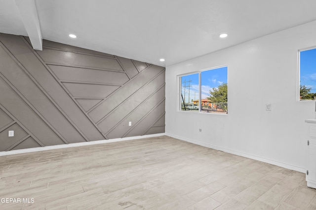 empty room with beamed ceiling, wooden walls, and light hardwood / wood-style flooring