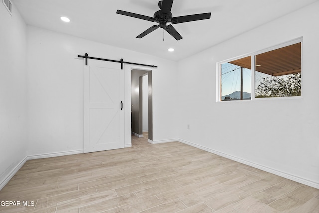 spare room with ceiling fan, light hardwood / wood-style floors, and a barn door