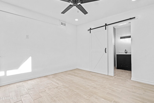 spare room with ceiling fan, light hardwood / wood-style flooring, and a barn door