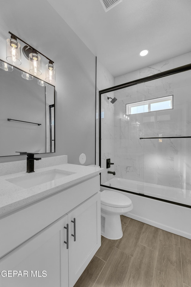 full bathroom featuring hardwood / wood-style floors, shower / bath combination with glass door, vanity, and toilet