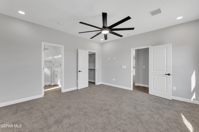 unfurnished bedroom featuring a walk in closet, ensuite bathroom, ceiling fan, a closet, and dark carpet