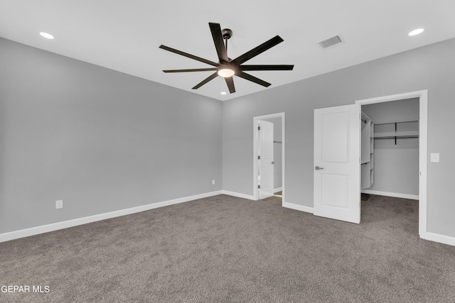 unfurnished bedroom with dark colored carpet, a closet, a walk in closet, and ceiling fan