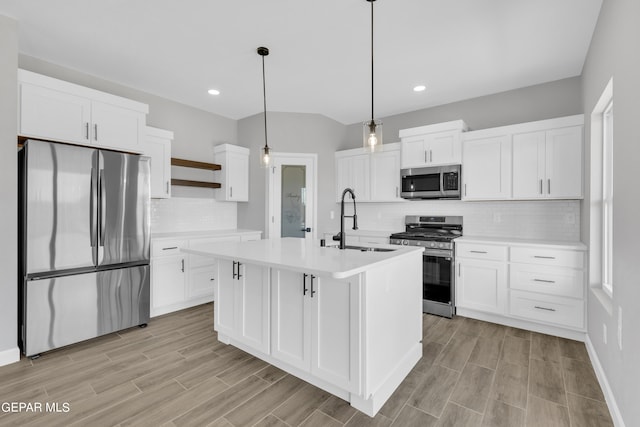 kitchen with pendant lighting, white cabinets, sink, a center island with sink, and appliances with stainless steel finishes