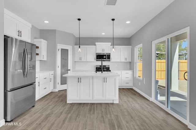 kitchen featuring white cabinets, decorative light fixtures, a kitchen island with sink, light hardwood / wood-style flooring, and appliances with stainless steel finishes