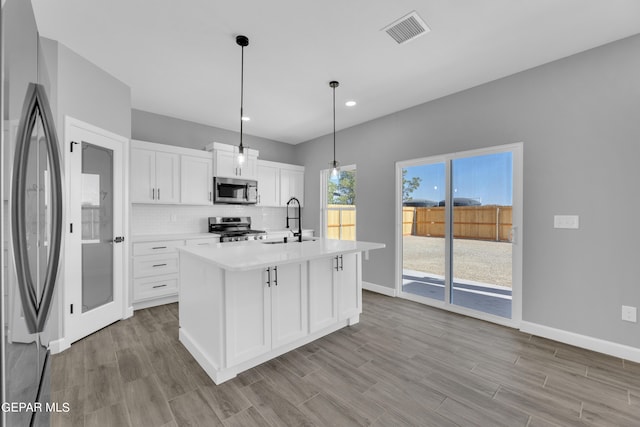 kitchen with hanging light fixtures, sink, a center island with sink, white cabinetry, and appliances with stainless steel finishes