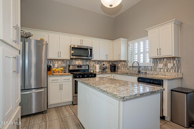 kitchen with stainless steel appliances, light stone countertops, backsplash, white cabinets, and a center island