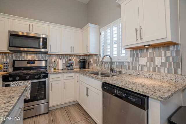 kitchen with light stone countertops, stainless steel appliances, tasteful backsplash, sink, and white cabinetry