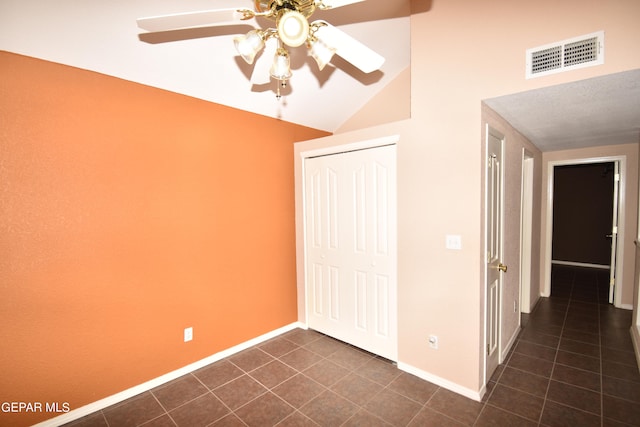 unfurnished bedroom with a closet, ceiling fan, vaulted ceiling, and dark tile patterned floors