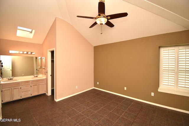 unfurnished bedroom featuring ceiling fan, dark tile patterned floors, connected bathroom, vaulted ceiling with skylight, and sink