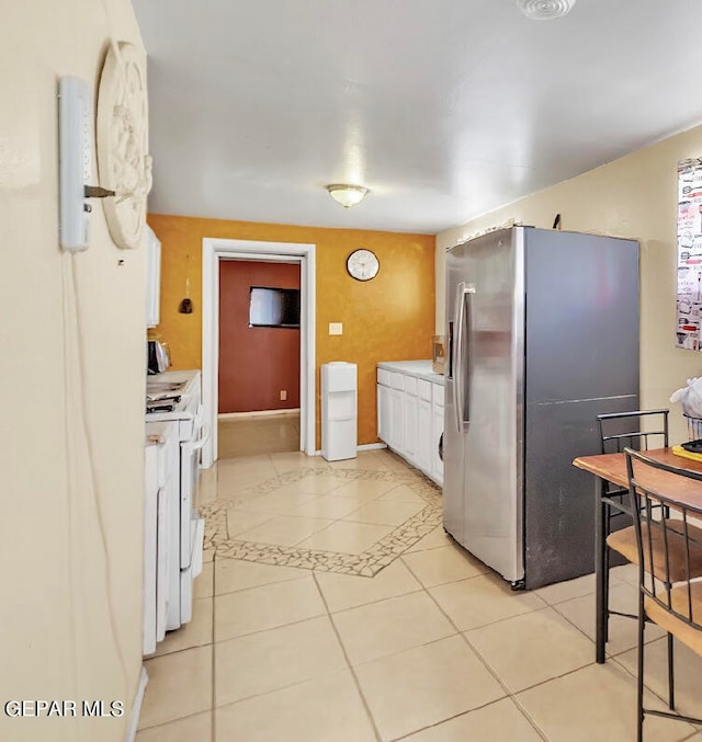 kitchen featuring white cabinetry, white stove, light tile patterned floors, and stainless steel refrigerator