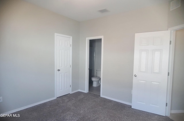 unfurnished bedroom with ensuite bathroom and dark colored carpet