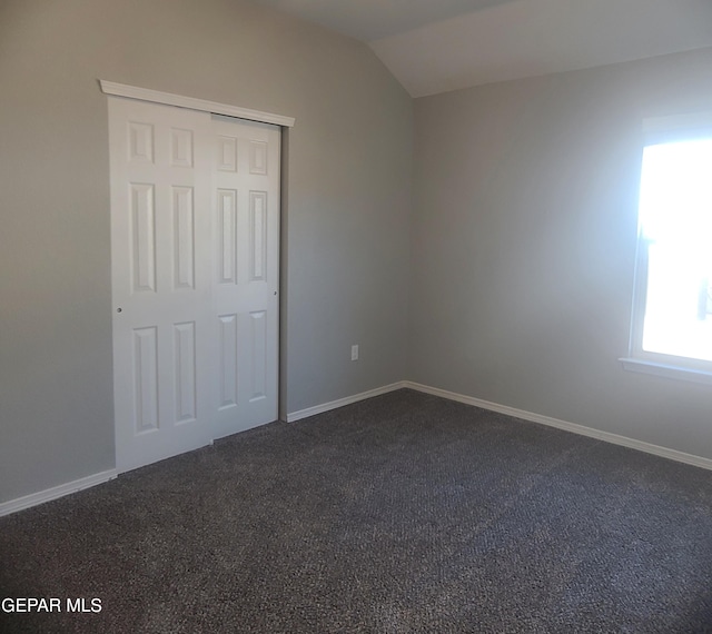 unfurnished bedroom featuring dark carpet, a closet, and vaulted ceiling