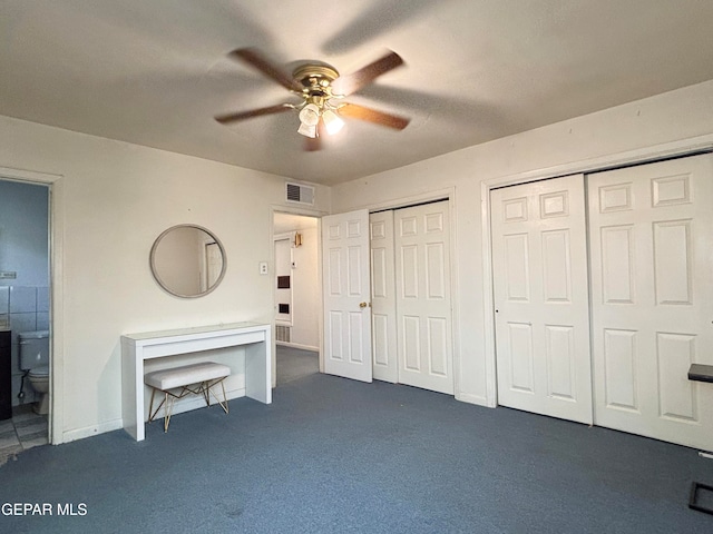 unfurnished bedroom with connected bathroom, dark colored carpet, multiple closets, and ceiling fan