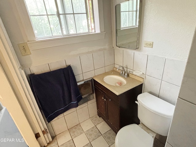 bathroom featuring vanity, toilet, tile walls, and a wealth of natural light