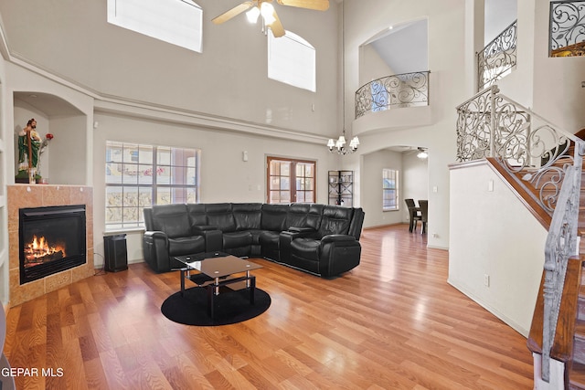 living room featuring a towering ceiling, hardwood / wood-style flooring, a tiled fireplace, and ceiling fan with notable chandelier