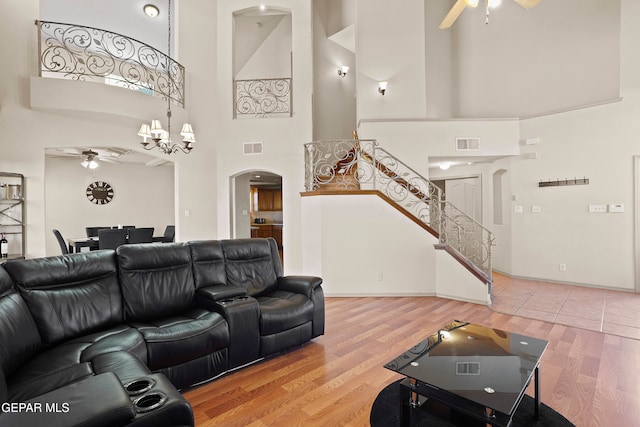 living room with a towering ceiling, hardwood / wood-style floors, and ceiling fan with notable chandelier