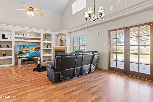 living room with built in shelves, hardwood / wood-style floors, ceiling fan with notable chandelier, and high vaulted ceiling