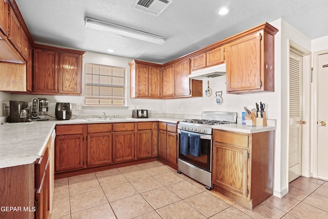 kitchen with sink, stainless steel range with gas cooktop, a textured ceiling, and light tile patterned floors