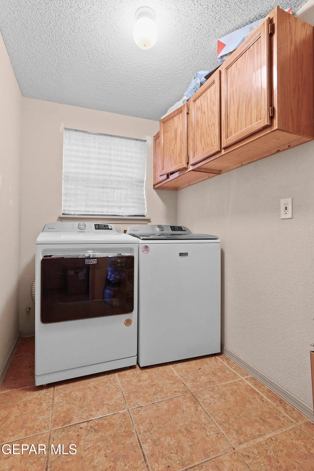 clothes washing area with cabinets, washer and dryer, a textured ceiling, and light tile patterned floors