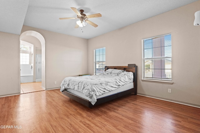 bedroom with multiple windows, ensuite bathroom, light wood-type flooring, and ceiling fan