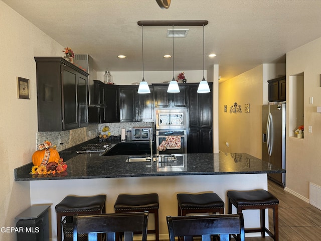 kitchen with pendant lighting, kitchen peninsula, tasteful backsplash, appliances with stainless steel finishes, and a kitchen bar