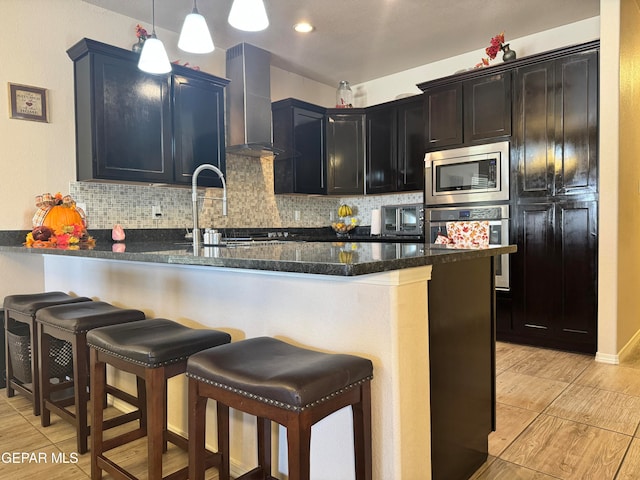 kitchen with wall chimney exhaust hood, stainless steel microwave, decorative light fixtures, kitchen peninsula, and backsplash