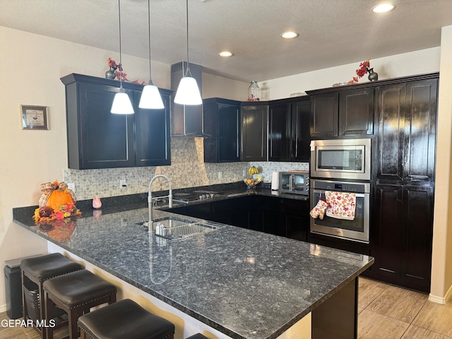 kitchen with pendant lighting, sink, tasteful backsplash, appliances with stainless steel finishes, and dark stone countertops