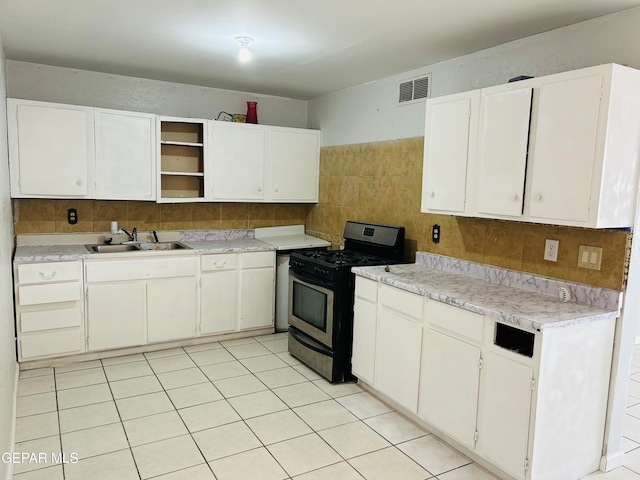 kitchen with sink, white cabinets, decorative backsplash, light tile patterned floors, and stainless steel gas range