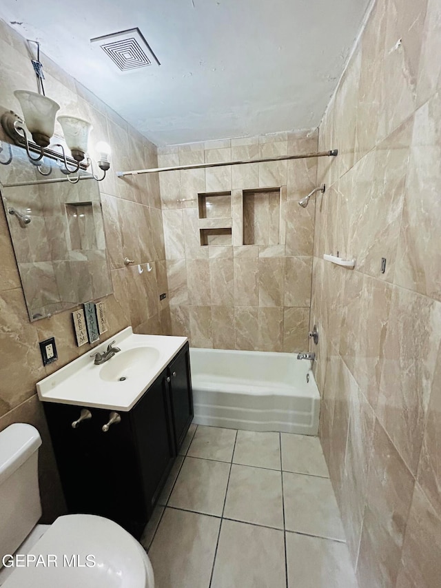 full bathroom featuring toilet, tile walls, vanity, tiled shower / bath combo, and tile patterned flooring