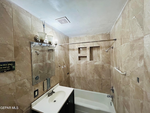 bathroom featuring tiled shower / bath, vanity, and tile walls