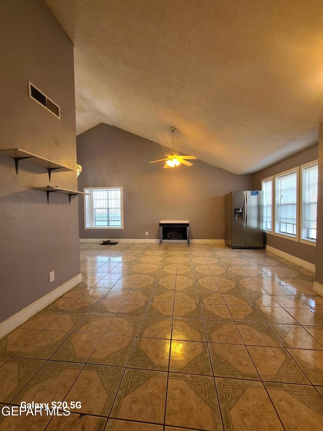 unfurnished living room with vaulted ceiling, ceiling fan, a healthy amount of sunlight, and light tile patterned flooring