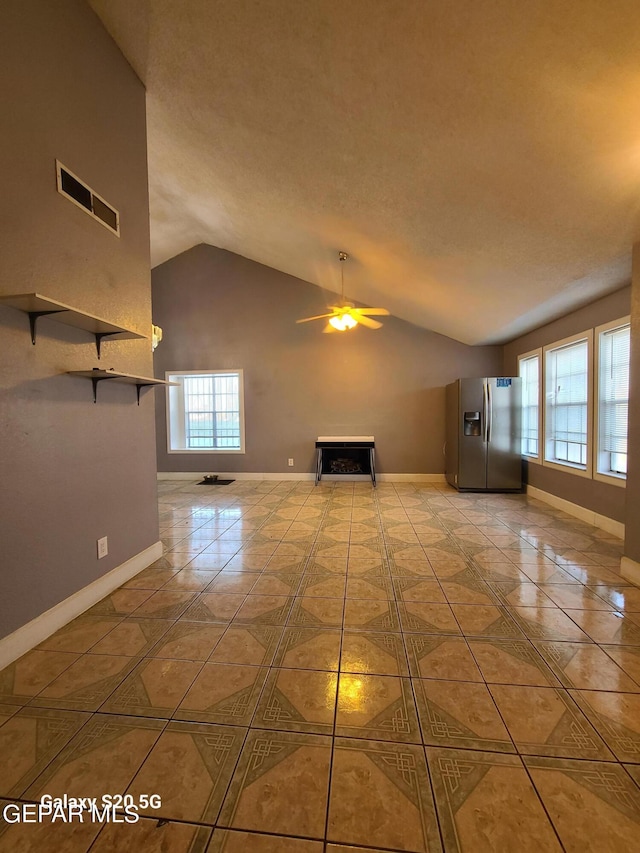 unfurnished living room with ceiling fan, light tile patterned floors, a wealth of natural light, and vaulted ceiling