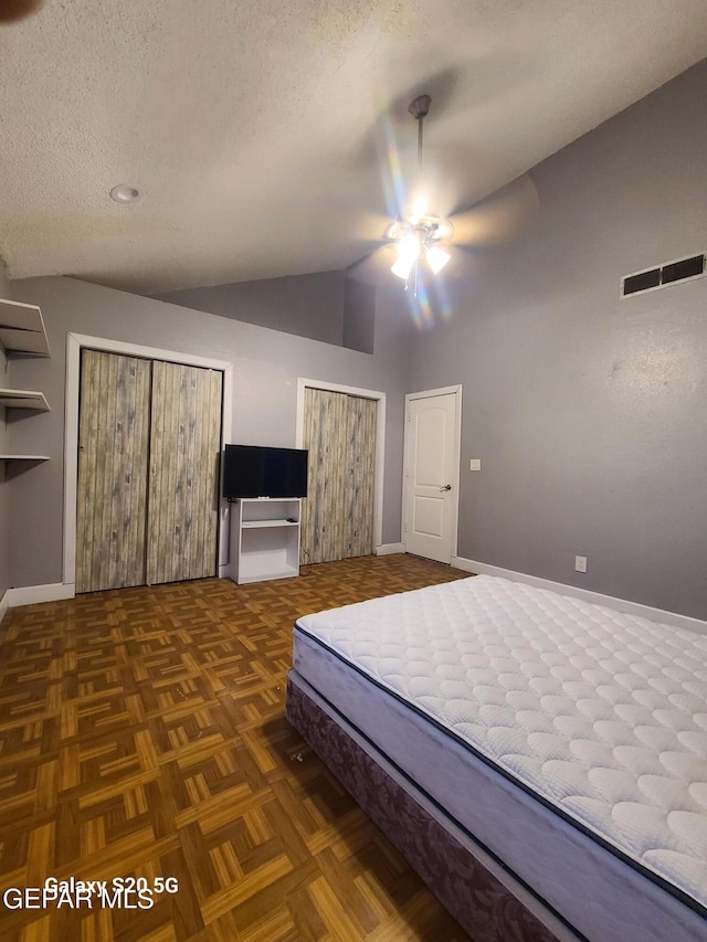 unfurnished bedroom with a textured ceiling, dark parquet floors, ceiling fan, and lofted ceiling