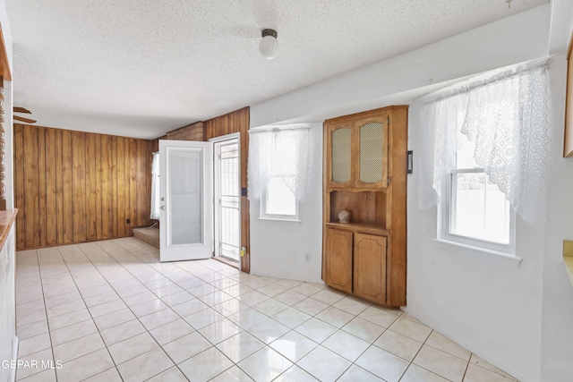 tiled empty room featuring ceiling fan, a textured ceiling, wood walls, and a healthy amount of sunlight