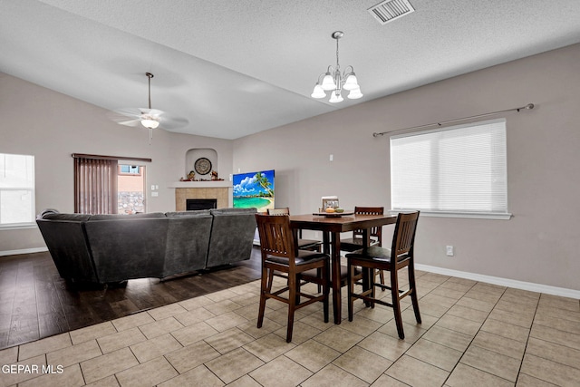 dining space featuring a fireplace, a textured ceiling, light wood-type flooring, and ceiling fan with notable chandelier